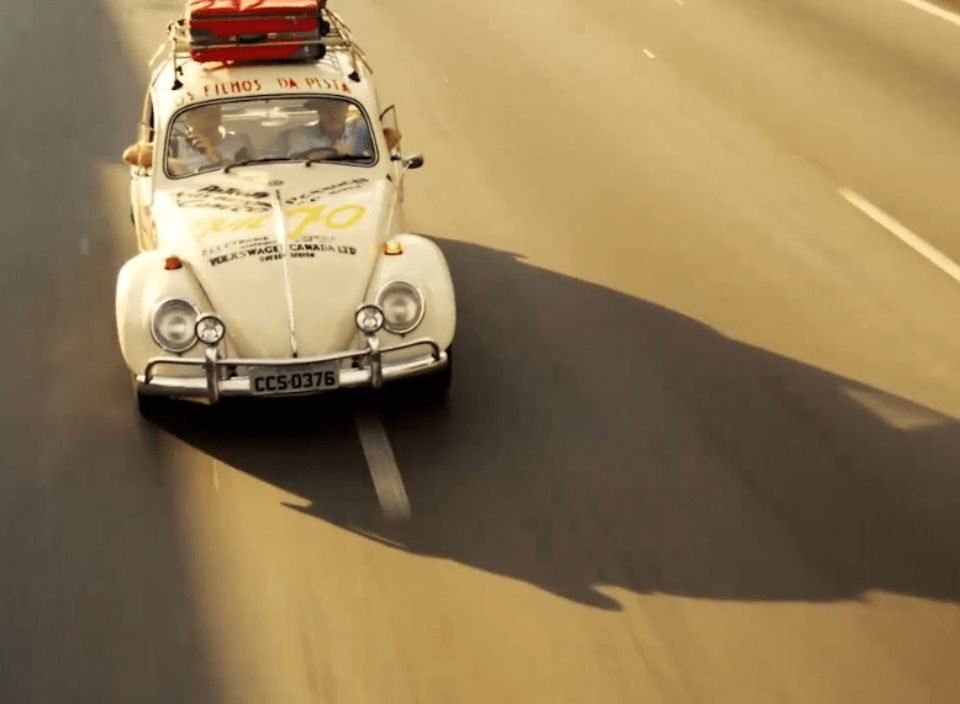 Um fusca branco fotografado na estrada, com sua sombra projetada no asfalto, num fim de tarde.