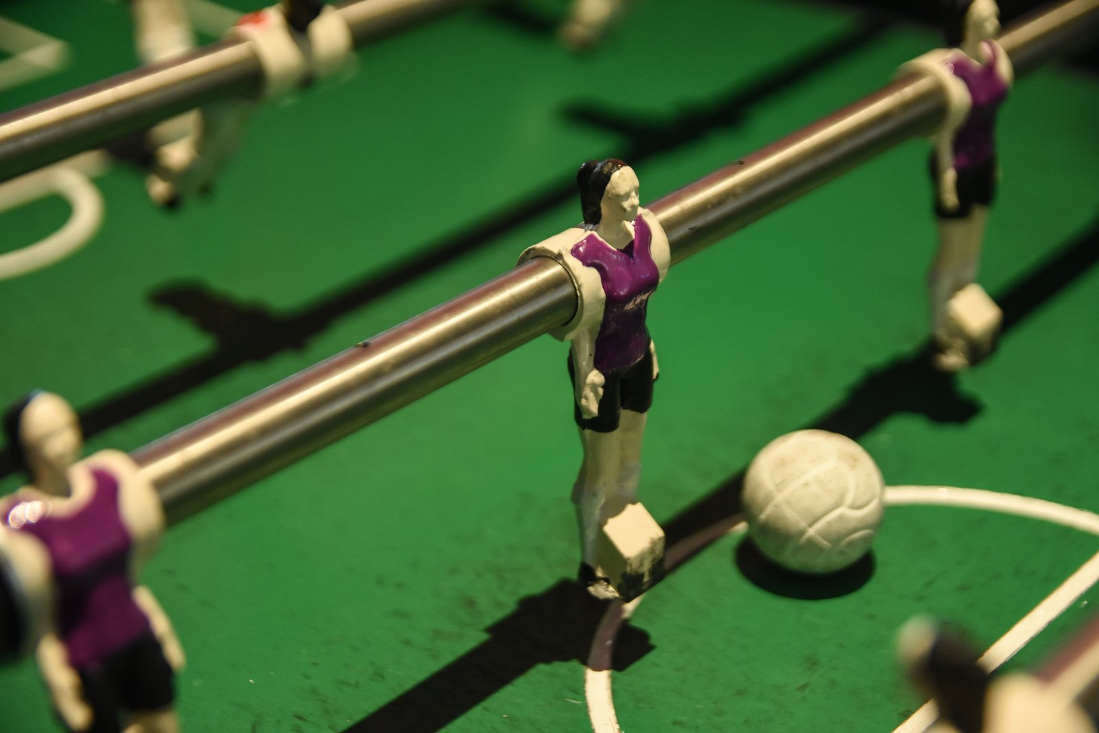 DSC_4805 Boneca de pebolim com uniforme roxo e calções pretos. Ao lado, uma bola de pebolim branca.