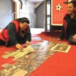 Pessoas sentadas no chão em uma sala colorida do Museu do Futebol. Estão montando um grande quebra cabeças