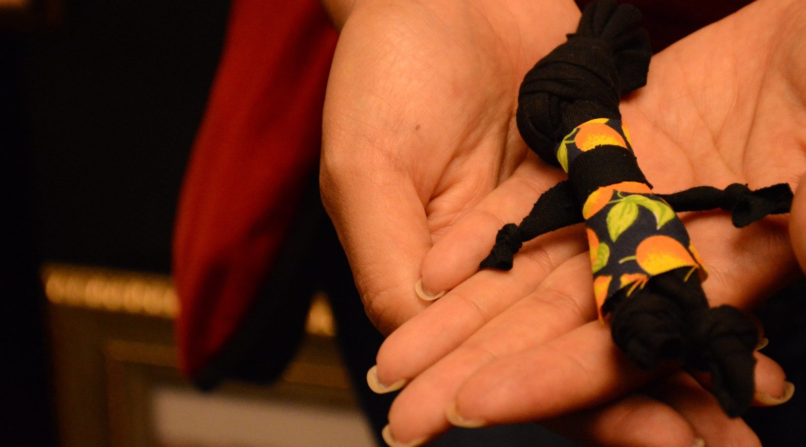 Close nas mãos de uma mulher que segura uma Abayomi, boneca negra feita de pano.