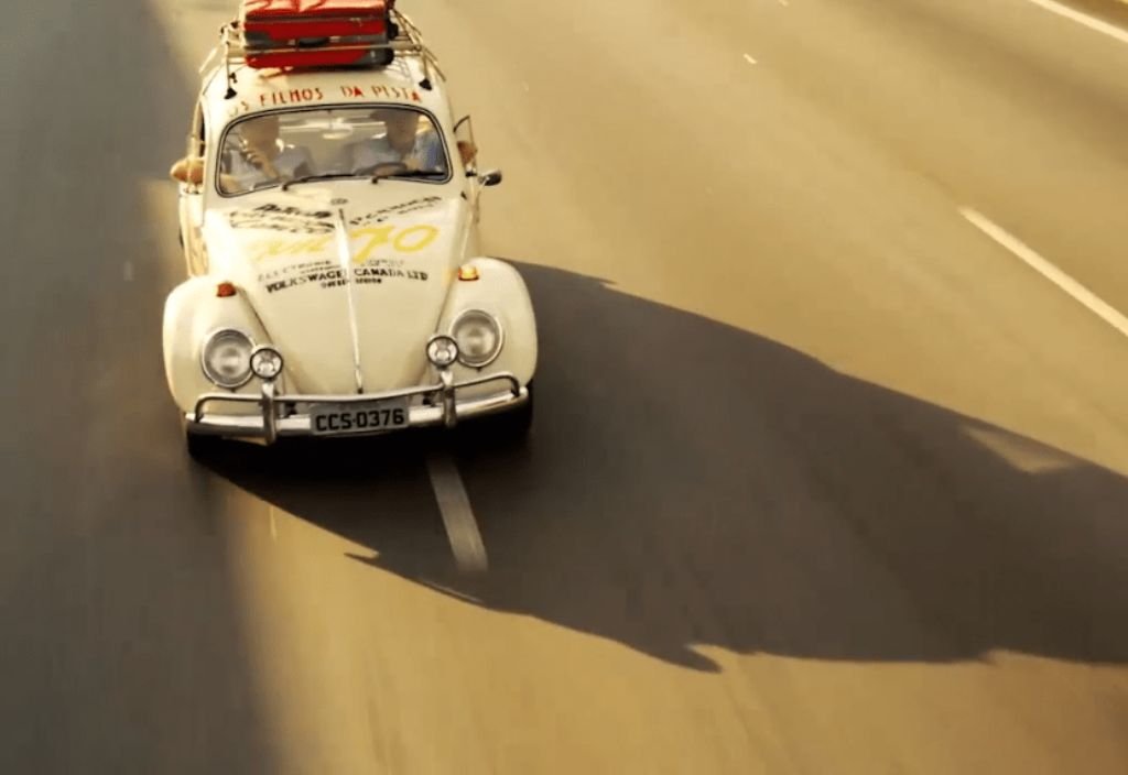 Um fusca branco fotografado na estrada, com sua sombra projetada no asfalto, num fim de tarde.