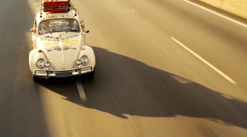 Um fusca branco fotografado na estrada, com sua sombra projetada no asfalto, num fim de tarde.