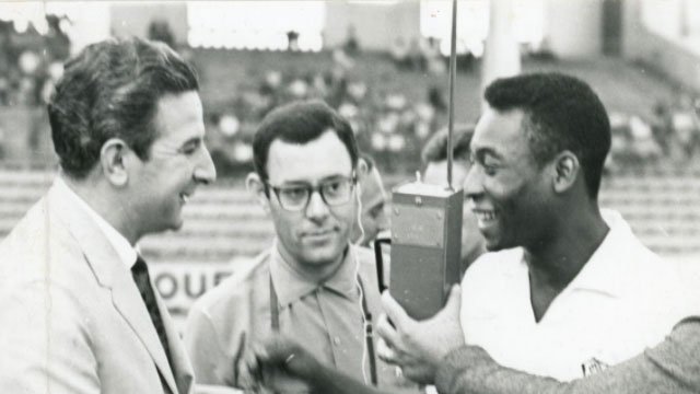 Foto em preto e branco de Pelé, sendo entrevistado por jornalistas em campo.