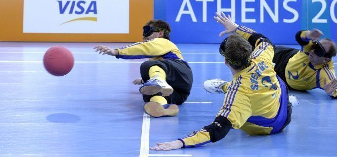 Três homens com vendas em uma quadra de esportes. A bola vem na direção de um deles.