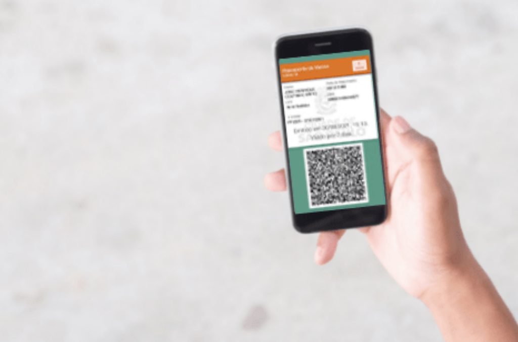 Foto de uma mão que segura o celular. A tela mostra o passaporte da vacina.