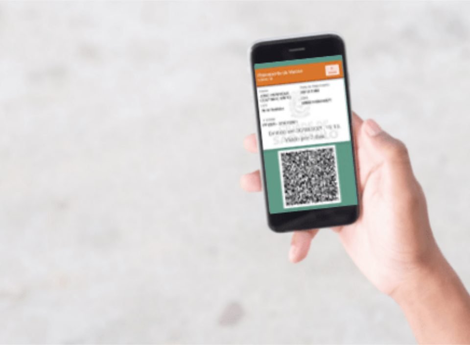Foto de uma mão que segura o celular. A tela mostra o passaporte da vacina.