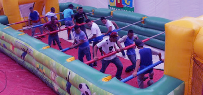 Um grupo de pessoas brinca dentro de uma grande estrutura inflável que imita um pebolim.