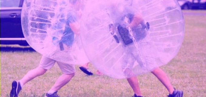 Duas pessoas envolvidas em um inflável em forma de bola se jogam uma contra a outra.