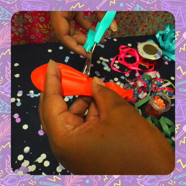 Uma pessoa corta uma bexiga vermelha com uma tesoura.