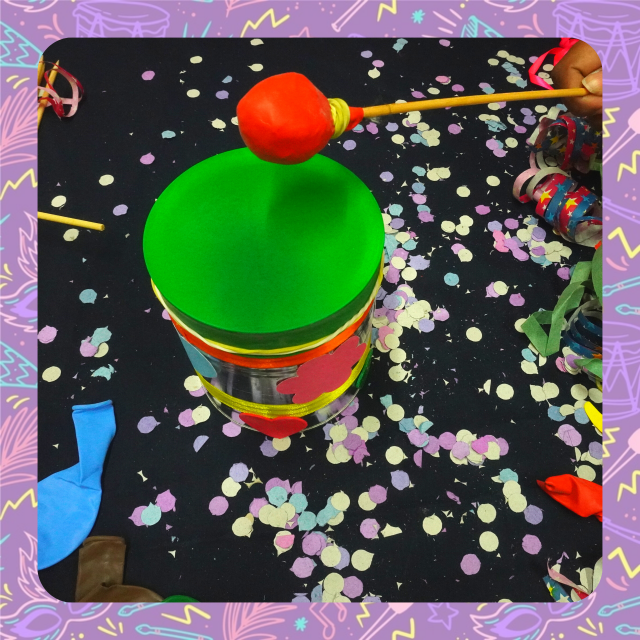 Imagem de um tampor de lata, com um tampo verde, e uma baqueta com a ponta vermelha