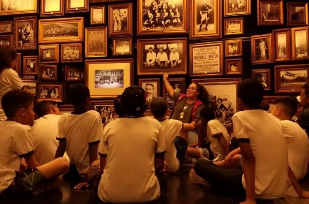 Imagem de um grupo de crianças e uma educadora do museu em uma sala com quadros