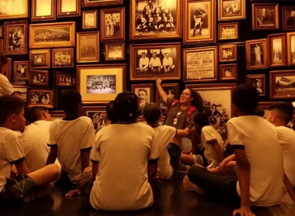 Imagem de um grupo de crianças e uma educadora do museu em uma sala com quadros