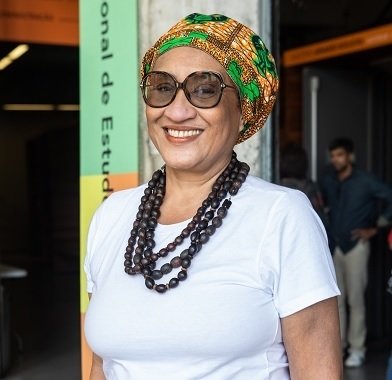 Claudia Silva Jacobs. Acervo Museu do Futebol _ Direitos Reservados Claudia veste uma blusa branca, colares com contas grandes e escuras, óculos escuros e um turbante colorido.