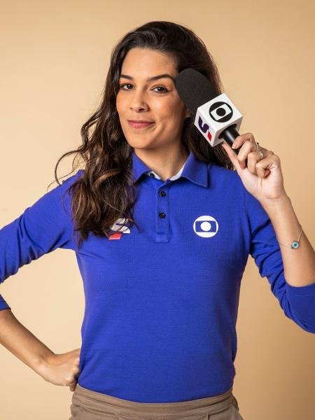 Renata Silveira. Reprodução. Renata Silveira veste o uniforme da Globo e SportV, que é uma camisa azul escura tipo polo de mangas compridas. Ela tem cabelo escuro, longo, e segura o microfone perto do rosto.