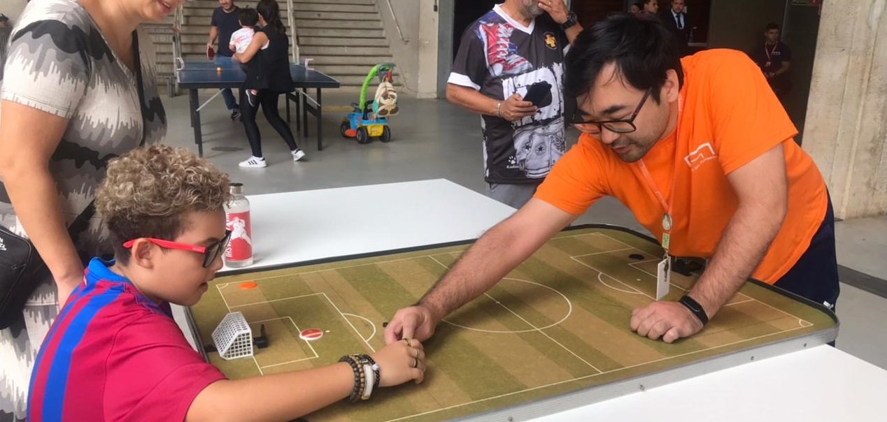 Imagem com um educador e uma criança com o futebol de botao