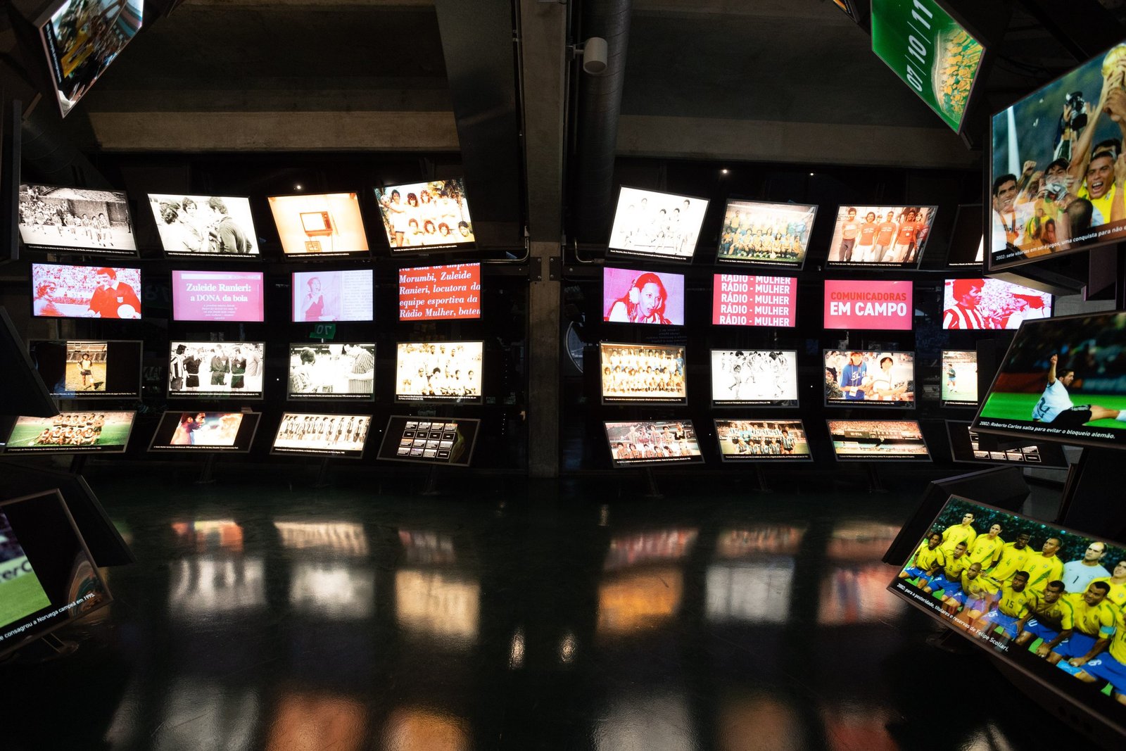 Sala com fotografias iluminadas retratando jogadores e jogadoras de futebol.