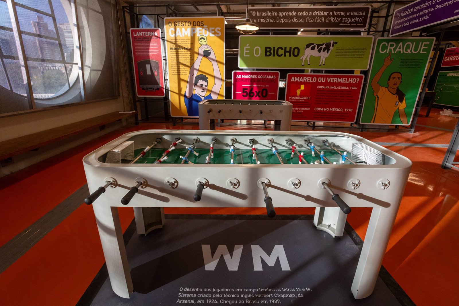 Museu do Futebol Imagem de uma mesa de pebolim dentro do museu iluminada pela luz natural que passa por uma janela redonda.