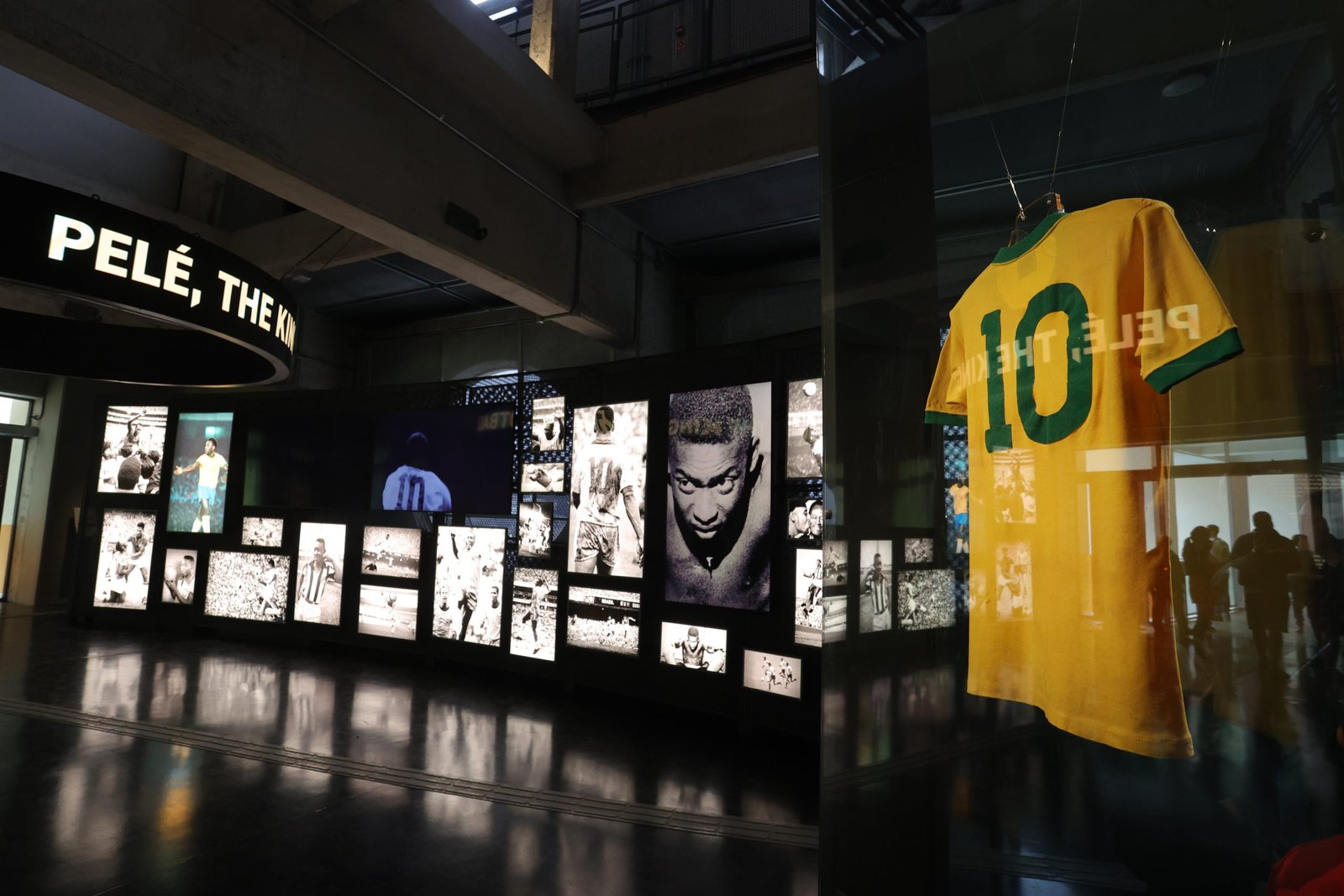 Em primeiro plano aparece a camisa 10 amarela usada por Pelé na Copa de 1970. No fundo há um painel com várias imagens iluminadas, fotos em preto e branco do Rei.