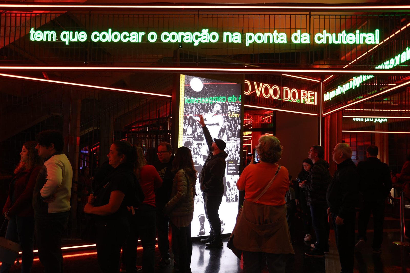 Museu Futebol Foto da sala Jogo de Corpo, mostrando vários espaçoso com luz neon. Ao fundo, um homem está em frente a uma foto de Pelé cabeceando uma bola em tamanho real, ele tenta alcançar a bola com a mão.