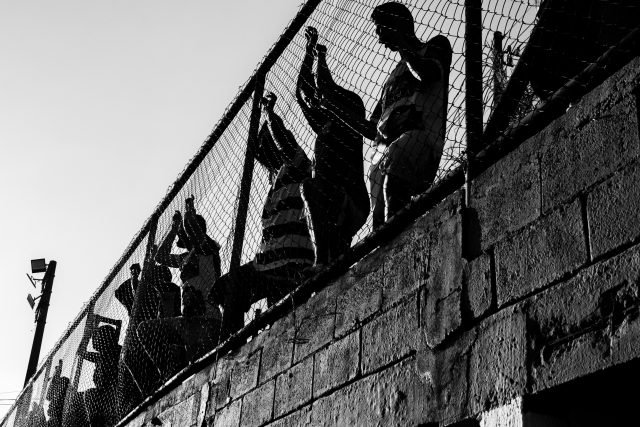 EvandroLima Imagem em preto e branco registra torcedores grudados ao alambrado assistindo à partida de futebol.
