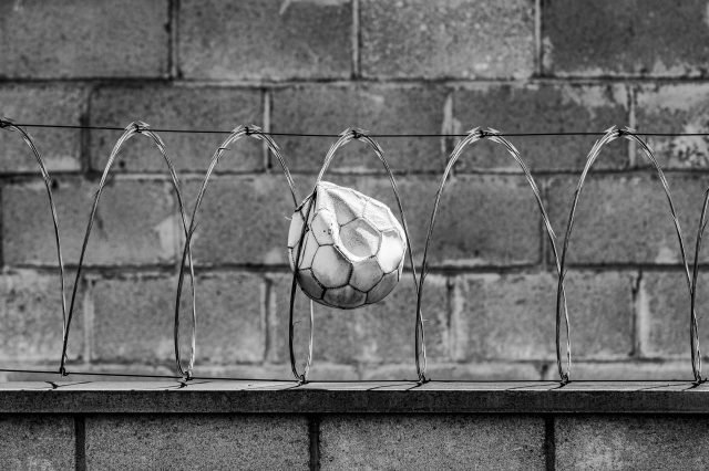 RodrigoPivas Imagem em preto e branco de uma bola presa na cerca de arame farpado.