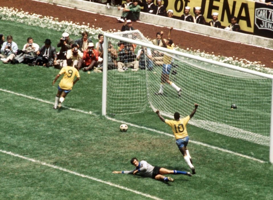 Pelé de costas levanta os braços em comemoração a um gol, com a bola ainda por passar a linha. O goleiro adversário está no chão.
