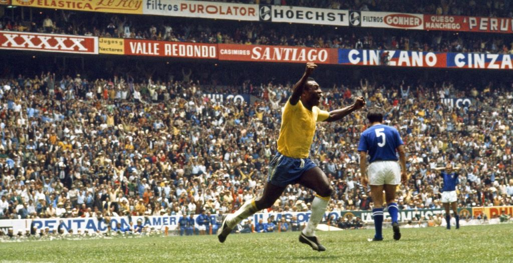 Pelé, vestido com a camisa da Seleção Brasileira, comemora um gol. Atrás dele há um estádio lotado.