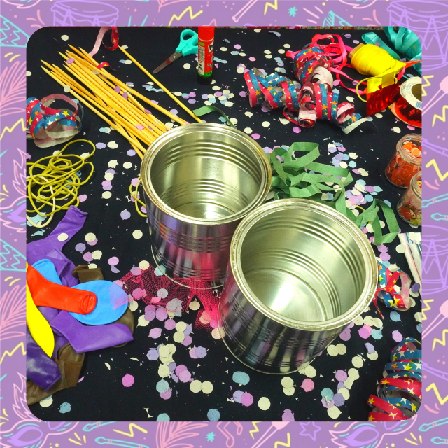A foto mostra duas latas, bexigas e elásticos, sobre uma mesa cheia de confetes de carnaval