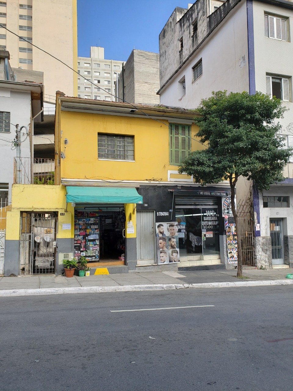 Foto de uma rua com casas brancas e amarela, e prédios ao fundo