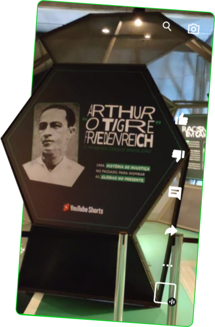 Imagem da entrada da instalação, uma grande placa hexagonal com foto de rosto de Friedenreich e as palavras "Arthur O Tigre Friedenreich"