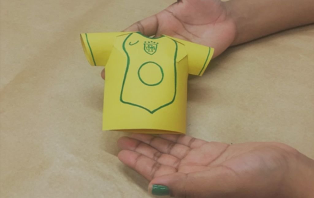 imagem com uma mão, ensinando fazer camisas de papel