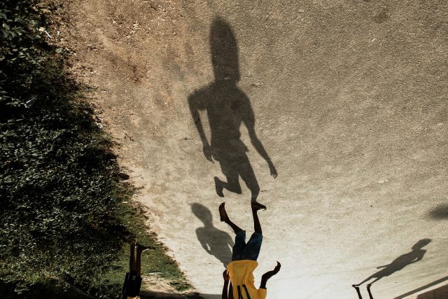 Foto da sombra de uma criança jogando bola. A imagem está invertida; vemos a sobra de pé e a criança de cabeça para baixo, com a camisa amarela da Seleção Brasileira.