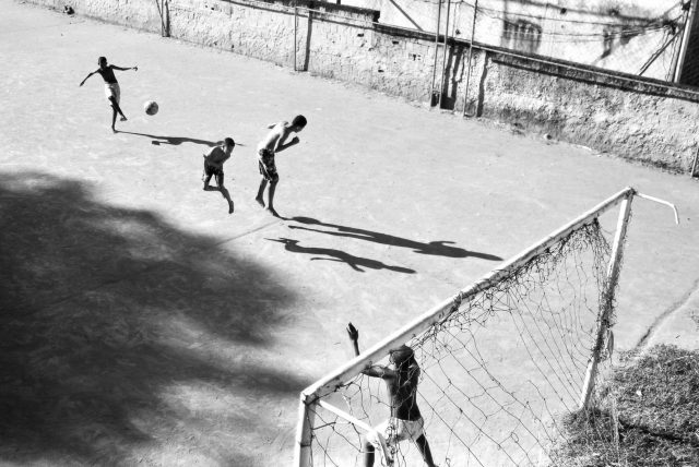 Imagem em preto e branco de crianças jogando bola em uma quadra de concreto.