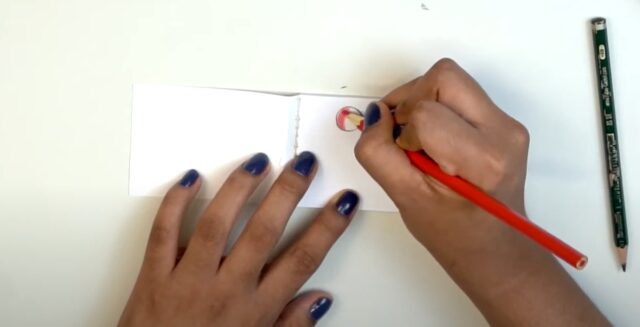 Uma mão desenha em um papel com um lápois vermelho