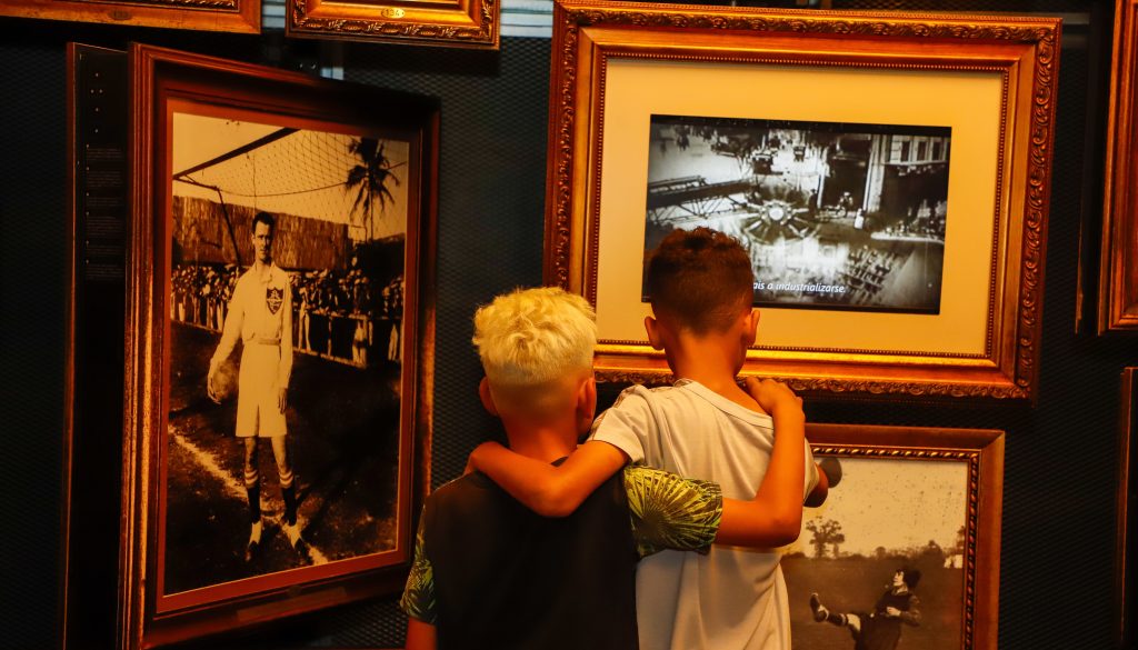 Imagem de dois garotos abraçados durante uma visita educativa, olhando as imagens da Sala Origens