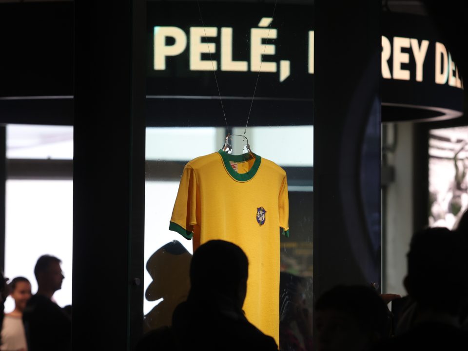 A camisa amarela de Pelé aparece ao fundo da imagem. Sobre ela, se lê um letreiro escrito "Pelé"