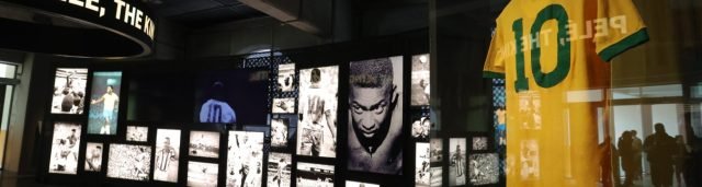 Imagem da Sala Pelé mostrando a camisa amarela número 10 em primeiro plano e, no fundo, fotografias do jogador em preto e branco.