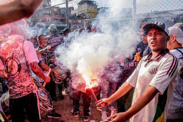 Torcedores comemoram. O torcedor principal segura um sinalizador, outros, com tambores, compõem a festa.