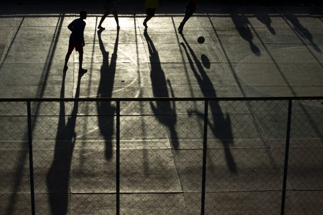 Foto em preto e branco. O destaque vai para as sombras das pessoas jogando futebol.