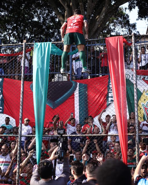 Pendurado no alambrado um jogador comemora a vitória ou título com a torcida.