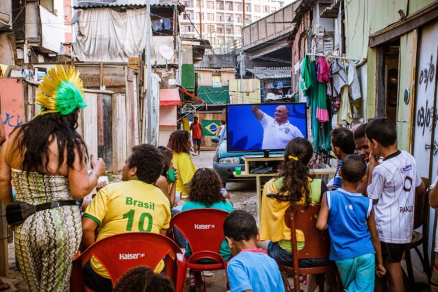 159_FOTO_GabrielCabral-GabrielCabral Em uma favela, um grupo de amigos ou familares assiste a um jogo de copa do mundo numa TV colocada no meio da rua.