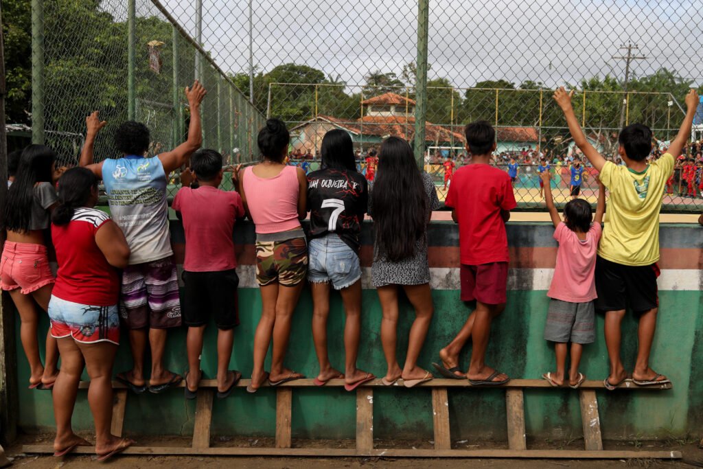 BRAZIL Pessoas de costas usam uma escada de madeira deitada de lado para conseguirem ver um jogo de futebol amador através de um muro