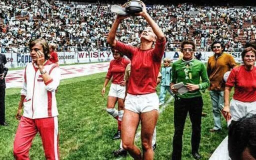 imagem em um campo. no centro, uma jogadora levanta a taça