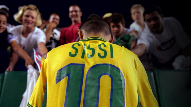 Imagem da jogadora Sissi, vestindoa camisa da seleção e de costas, autografando