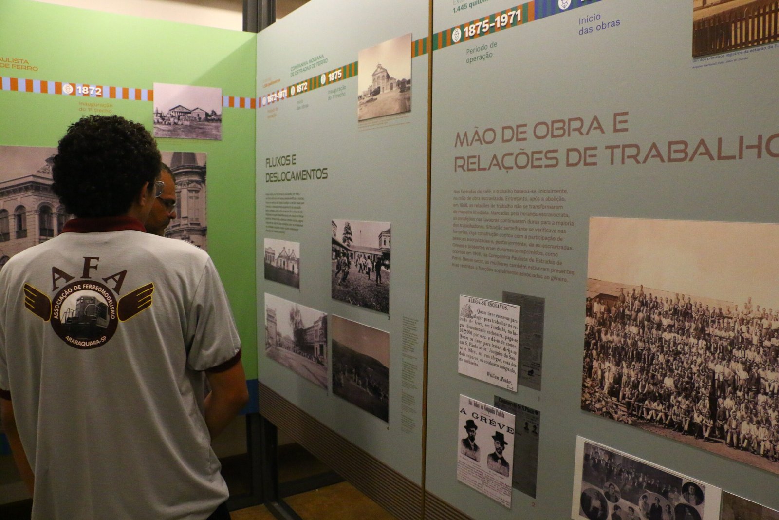 Imagem de um homem de costas, contemplando os painéis da exposiçao que tem textos e fotos.