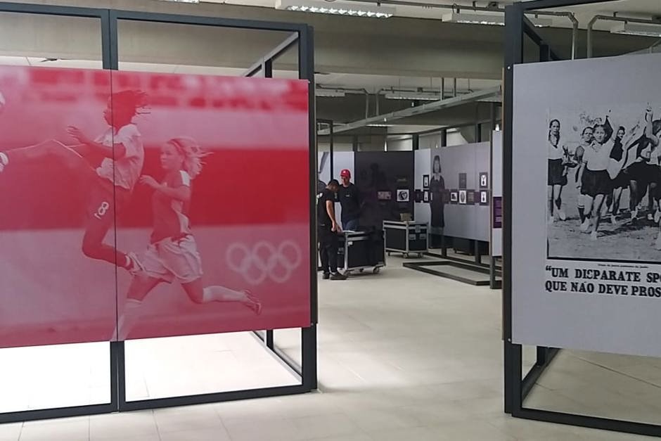 sjk Imagem da exposição Contra Ataque em São José dos Campos. Há painéis ao fundo com mulheres jogando futebol.