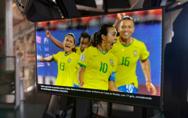 Imagem da Sala das Copas. Uma das telas representa jogadoras da seleção feminina comemorando gol. No centro, a Rainha Marta.