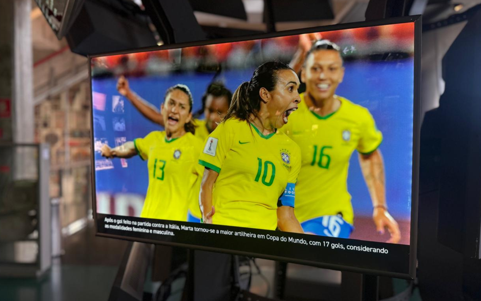 Imagem da Sala das Copas. Uma das telas representa jogadoras da seleção feminina comemorando gol. No centro, a Rainha Marta.