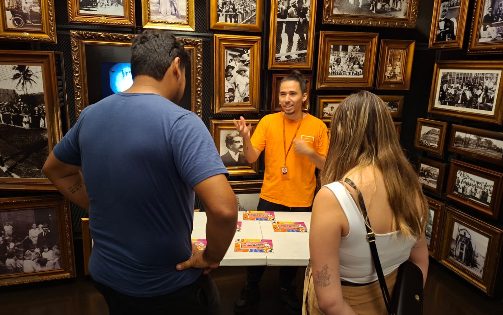 Foto da ativiade na Sala Origens; Educador está a frente de dois visitantes, realizando a atividade.
