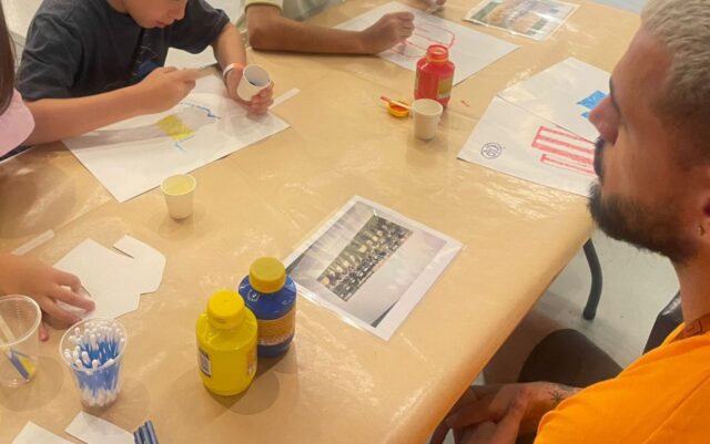 imagem - foto da tividad Oficina de Pontilhismo. N amesa o educador ensina crianças a atividade